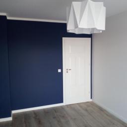 Wojewoda Jakub - Pomalowane na granatowo ściany w pokoju z białymi drzwiami i geometryczną lampą z papieru, widoczne panele podłogowe.