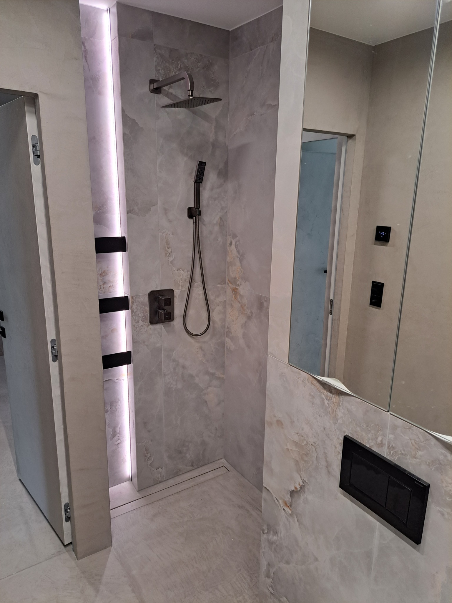 Nowoczesna łazienka z deszczownicą i panelami imitującymi marmur, podświetlona listwa LED, czarna armatura i minimalistyczny design.