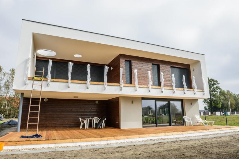 Nowoczesny dom dwukondygnacyjny z drewnianą elewacją, balkonem z okrągłymi świetlikami i częściowo zamontowanymi roletami, ze złożoną drabiną opartą o ścianę