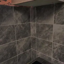 Fragment kuchni z szarymi marmurkowymi płytkami ściennymi, widoczny narożnik i krawędź szafki wiszącej, oraz fragment płyty kuchennej.