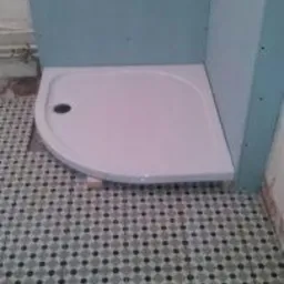 Brodzik narożny zamontowany w rogu łazienki, widoczne płyty kartonowo-gipsowe na ścianach, przygotowane do dalszych prac wykończeniowych.