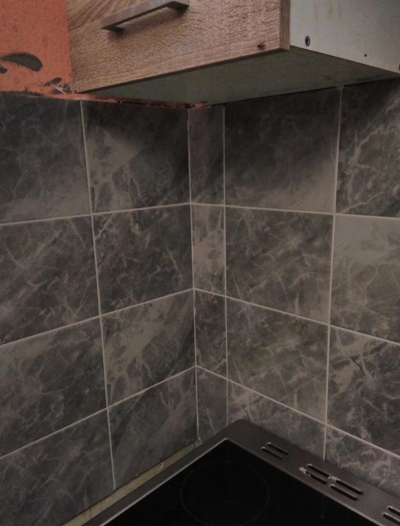 Fragment kuchni z szarymi marmurkowymi płytkami ściennymi, widoczny narożnik i krawędź szafki wiszącej, oraz fragment płyty kuchennej.