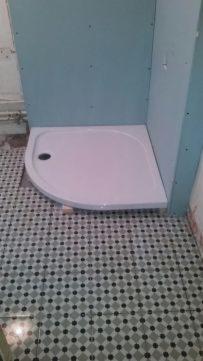 Brodzik narożny zamontowany w rogu łazienki, widoczne płyty kartonowo-gipsowe na ścianach, przygotowane do dalszych prac wykończeniowych.