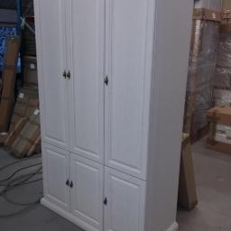 Zakład Stolarski Tadeusz Chodera - Biała szafa trzydrzwiowa z drewnianym blatem w magazynie, widoczne kartony w tle.