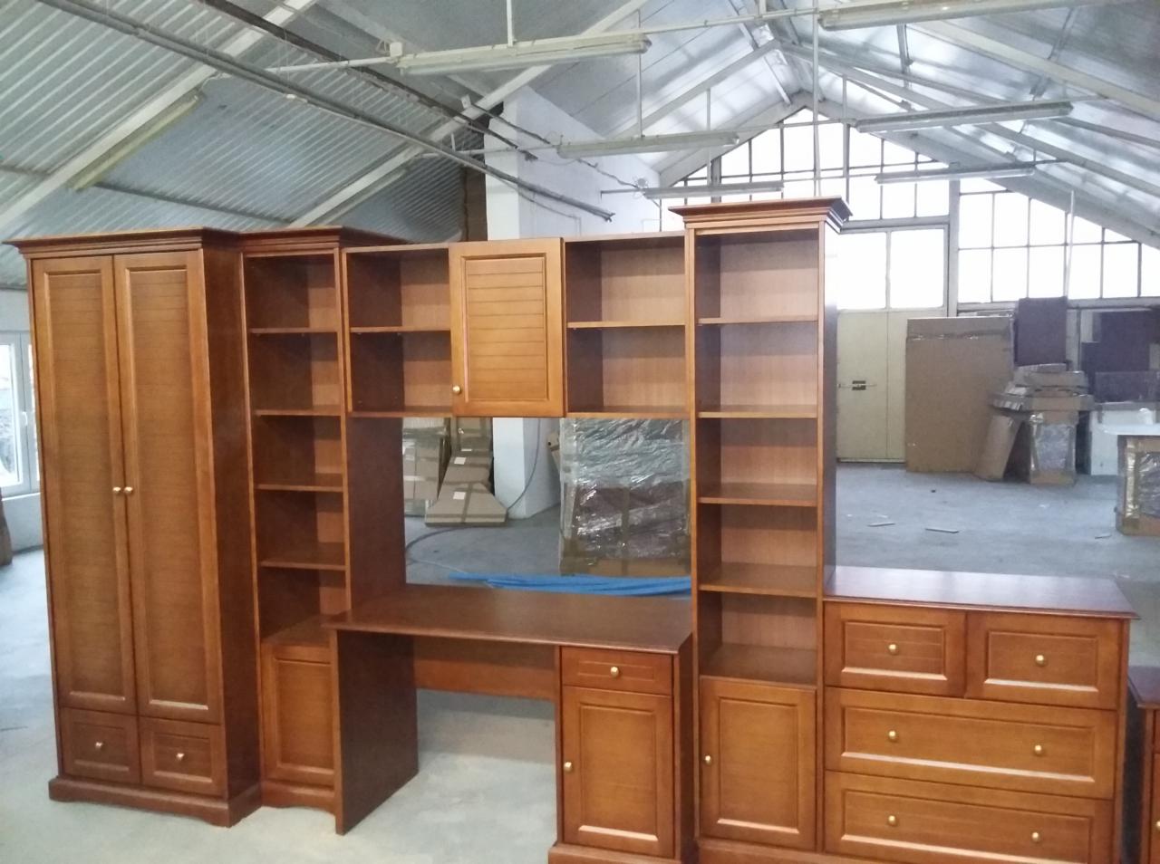 Zestaw drewnianych mebli: szafa dwudrzwiowa, regały otwarte, biurko z szafkami i komoda z szufladami, w surowym wnętrzu magazynu.