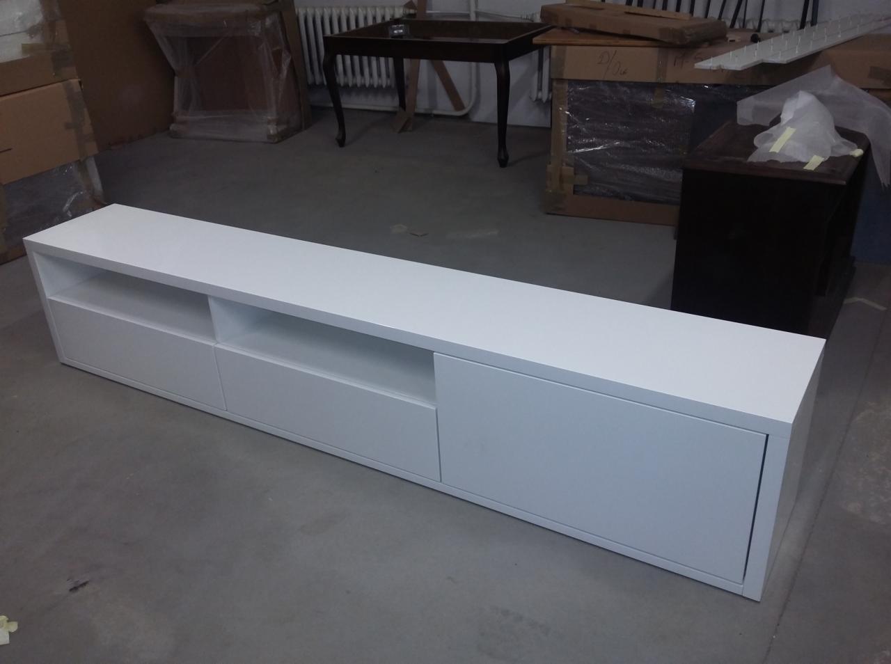 Biała, długa szafka RTV z szufladami i otwartymi półkami, sfotografowana w pomieszczeniu z kartonami i innymi meblami w tle.