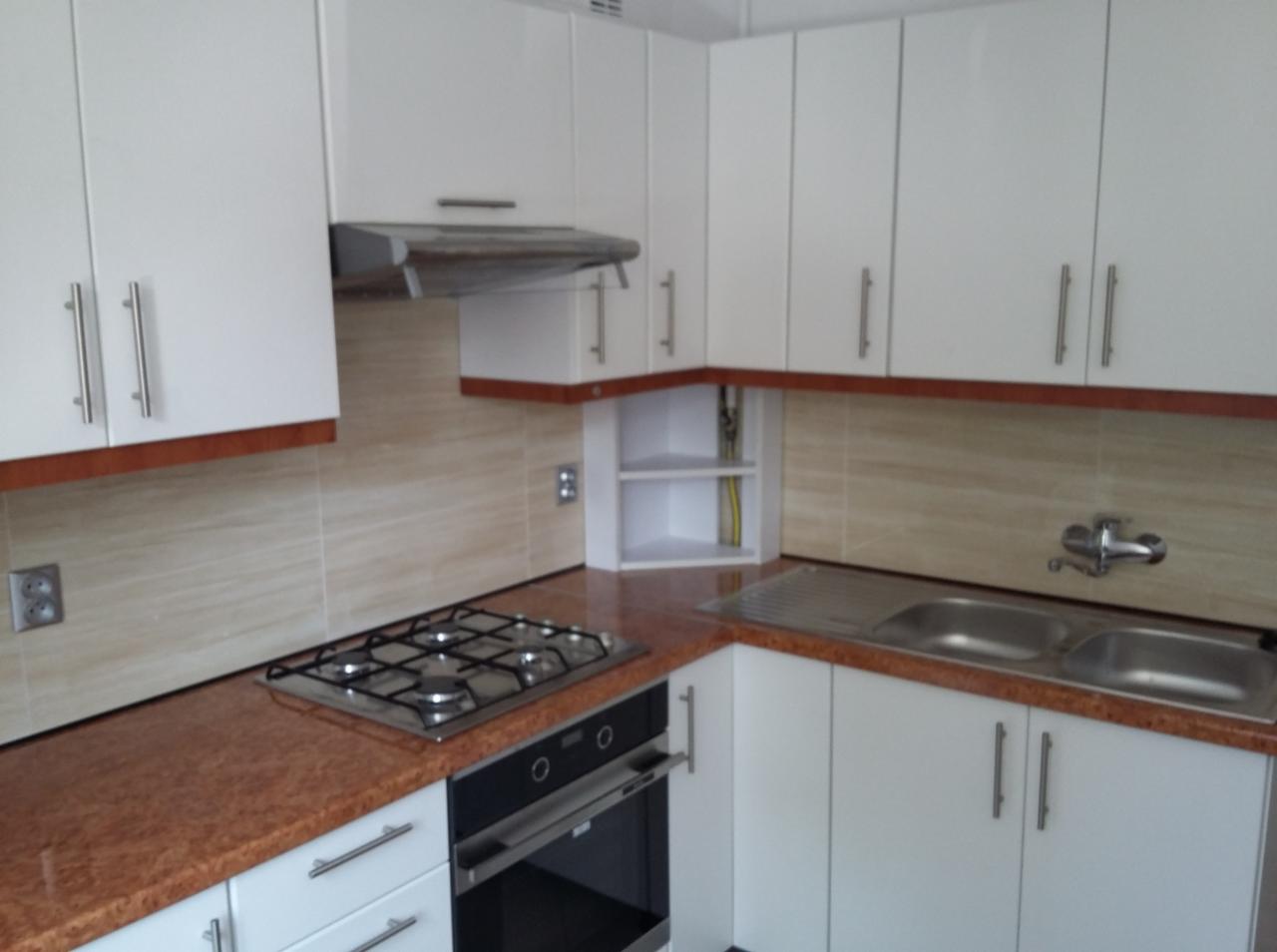 Jasna kuchnia z białymi szafkami, brązowym blatem i płytkami imitującymi kamień, widoczna płyta gazowa i zlewozmywak dwukomorowy.