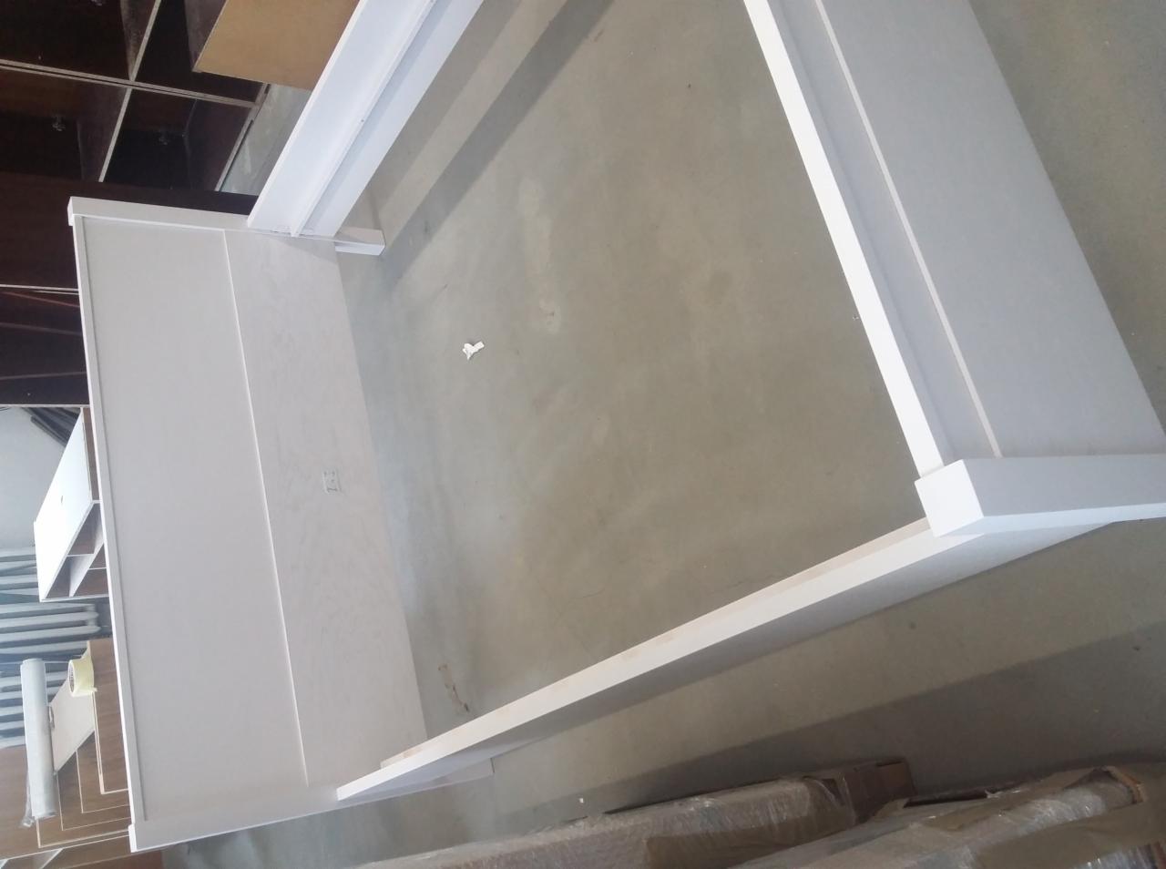 Biała rama meblowa w trakcie montażu, widoczne elementy konstrukcyjne i surowa podłoga w tle.