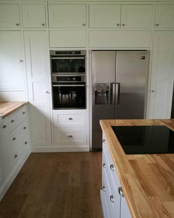 Jasna kuchnia z zabudową pod sufit, drewniany blat i nowoczesna lodówka dwudrzwiowa z dystrybutorem wody.