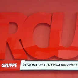 Czerwone, przestrzenne logo 'RCU' nad napisem 'VIVZ GRUPPE REGIONALNE CENTRUM UBEZPIECZEŃ' na czerwonym tle.