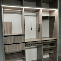 CHISEL KUCHNIE Agnieszka Kowalicka - Wnętrze nowoczesnej szafy z przesuwnymi drzwiami, oświetleniem LED i drewnianymi półkami, szufladami i drążkami na ubrania.