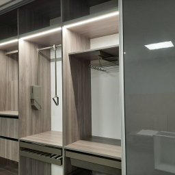 CHISEL KUCHNIE Agnieszka Kowalicka - Wnętrze nowoczesnej szafy z przesuwnymi, grafitowymi drzwiami, oświetleniem LED podszafkowym, półkami i szufladami z teksturą drewna.