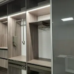 Wnętrze nowoczesnej szafy z przesuwnymi, grafitowymi drzwiami, oświetleniem LED podszafkowym, półkami i szufladami z teksturą drewna.