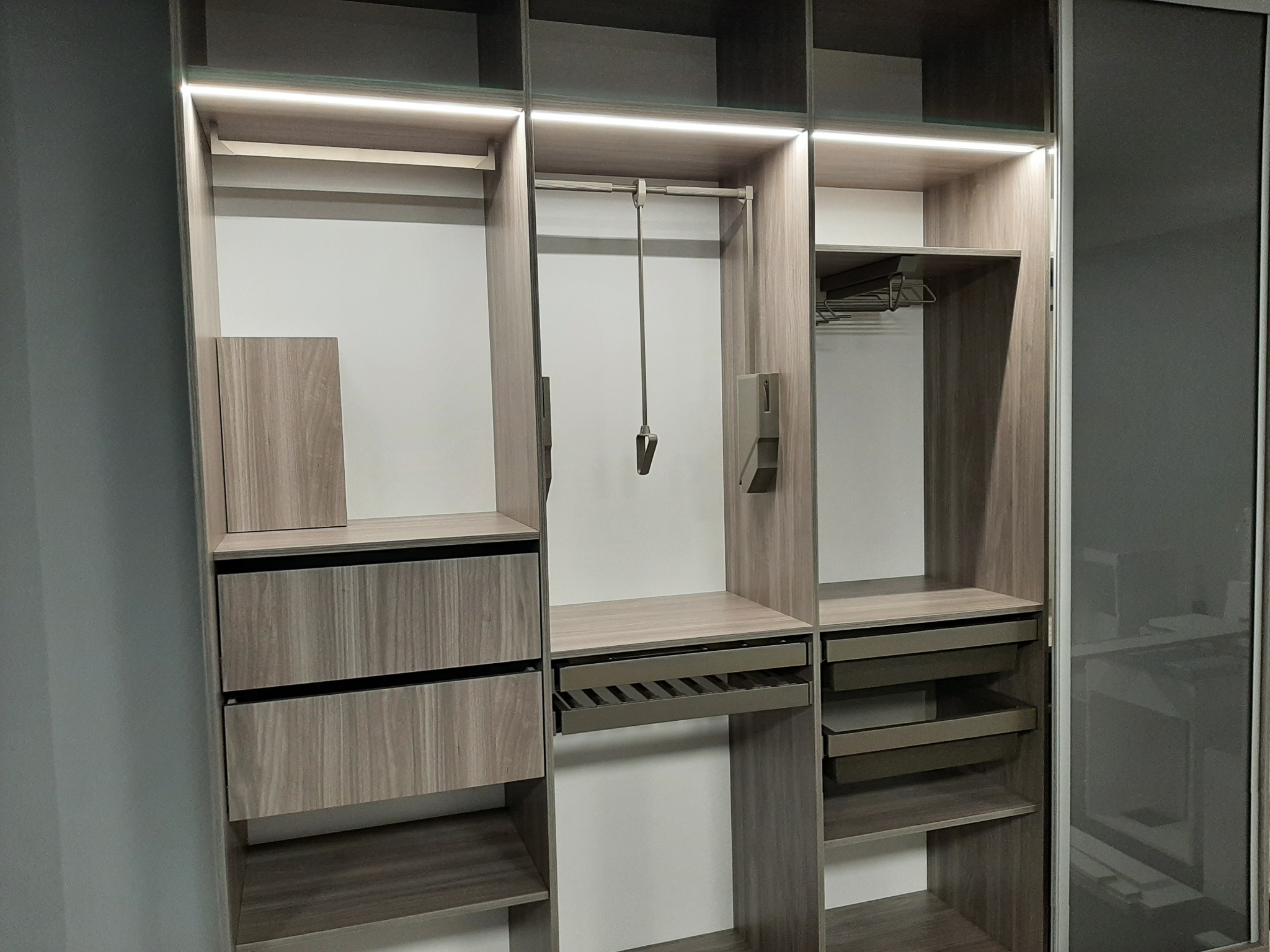 Wnętrze nowoczesnej szafy z przesuwnymi drzwiami, oświetleniem LED i drewnianymi półkami, szufladami i drążkami na ubrania.