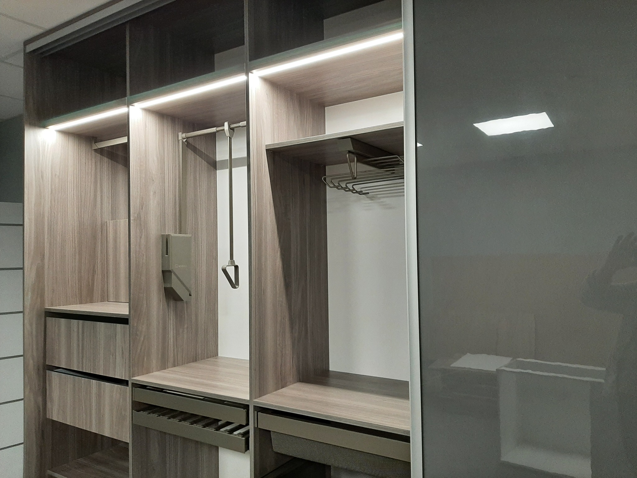 Wnętrze nowoczesnej szafy z przesuwnymi, grafitowymi drzwiami, oświetleniem LED podszafkowym, półkami i szufladami z teksturą drewna.