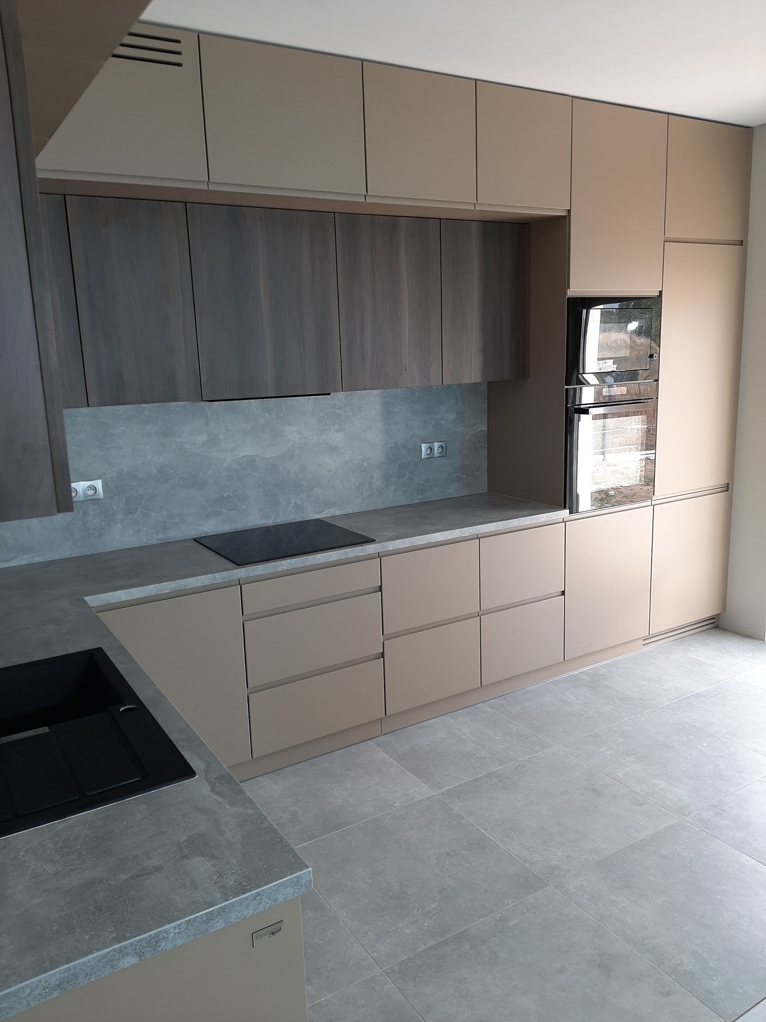 Nowoczesna kuchnia z beżowymi szafkami i szarym blatem, widok z perspektywy podłogi, minimalistyczny design, płyta indukcyjna i piekarnik w zabudowie.