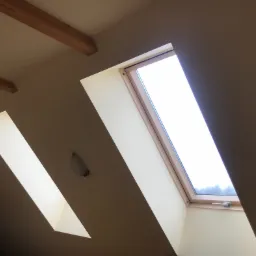 Wnętrze poddasza z dwoma oknami dachowymi, widok z dołu, z widoczną lampą sufitową i drewnianymi belkami konstrukcyjnymi.