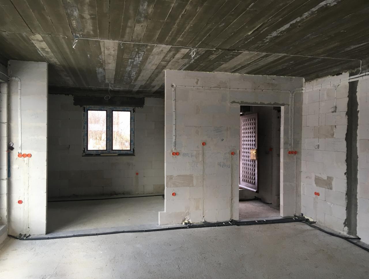 Surowy stan wnętrza budynku w trakcie prac elektrycznych: widoczne kable prowadzone po podłodze, puszki instalacyjne na ścianach z betonu komórkowego, okablowanie pod sufitem.