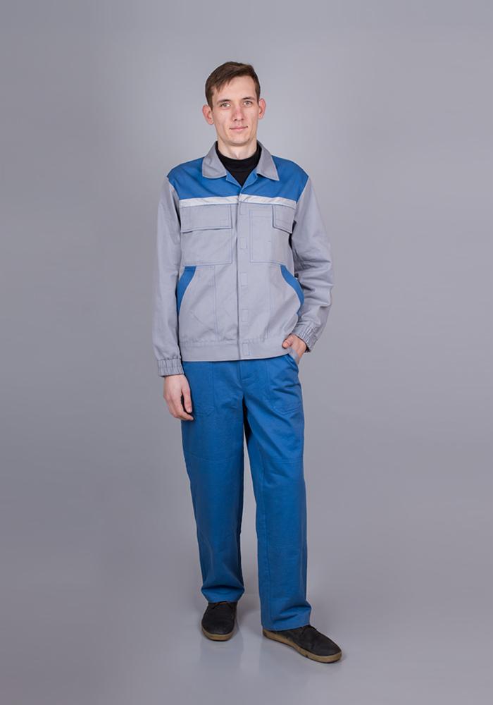 Mężczyzna w szaro-niebieskim uniformie roboczym, stojący na szarym tle, z ręką w kieszeni spodni.