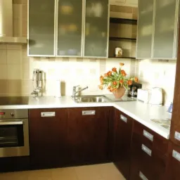 Nowoczesna kuchnia z ciemnobrązowymi szafkami i białym blatem, górne szafki z matowego szkła, na blacie wazon z tulipanami i akcesoria kuchenne.