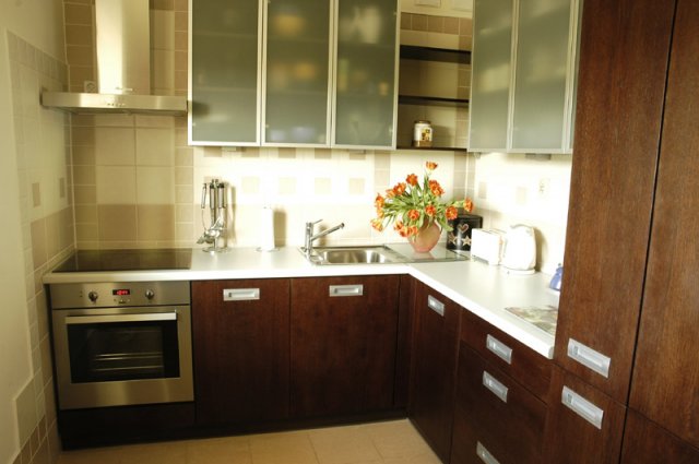 Nowoczesna kuchnia z ciemnobrązowymi szafkami i białym blatem, górne szafki z matowego szkła, na blacie wazon z tulipanami i akcesoria kuchenne.