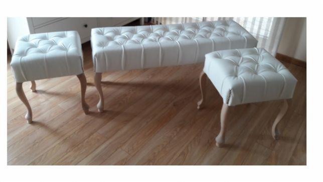 Komplet białych, pikowanych puf i ławki z drewnianymi, giętymi nogami na drewnianej podłodze. Widoczna faktura skóry ekologicznej i subtelne cieniowanie.