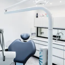 Nowoczesny, sterylny gabinet lekarski z szarym fotelem dentystycznym i białymi meblami, oświetleniem i narzędziami.