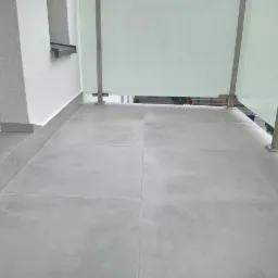 Szare płytki gresowe na balkonie w stanie deweloperskim, z widoczną balustradą ze stali nierdzewnej i matowego szkła.