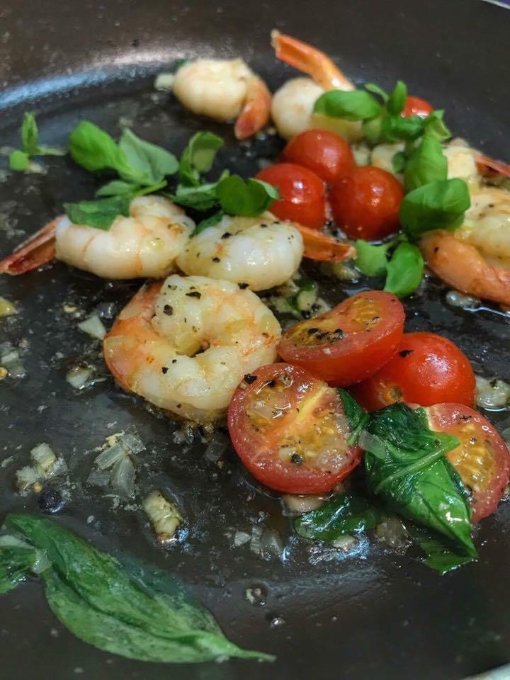 Smażone krewetki z pomidorkami cherry i bazylią na patelni, doprawione czarnym pieprzem i czosnkiem.