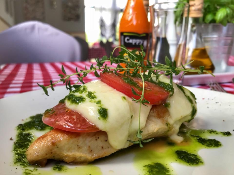 Filet z kurczaka zapiekany z serem mozzarella i pomidorem, polany pesto, udekorowany świeżym tymiankiem, na białym talerzu z czerwono-białą kratą w tle.