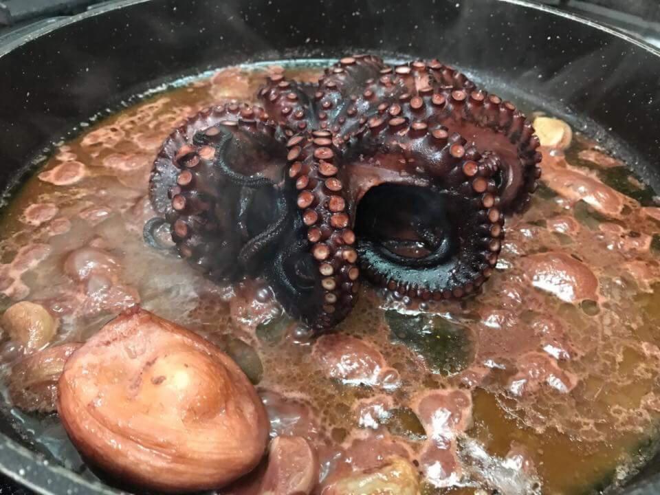 Gotowany ośmiornica w brązowym sosie z ziemniakami w czarnym garnku.