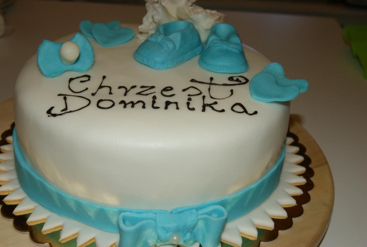 Tort na Chrzest Dominika z białym lukrem, błękitną wstążką i dekoracjami z masy cukrowej w kształcie bucików i serduszek.