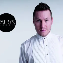 Portret mężczyzny w białej koszuli z czarnym logo 'Patryk Gnieździejko' na szarym tle, prezentujący profesjonalny wizerunek.
