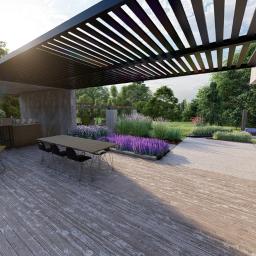 PERFORMA Patryk Gniedziejko - Nowoczesny taras z drewnianą podłogą, pergolą z czarnymi lamelami, grillem i leżakami, otoczony zielenią i fioletowymi kwiatami.
