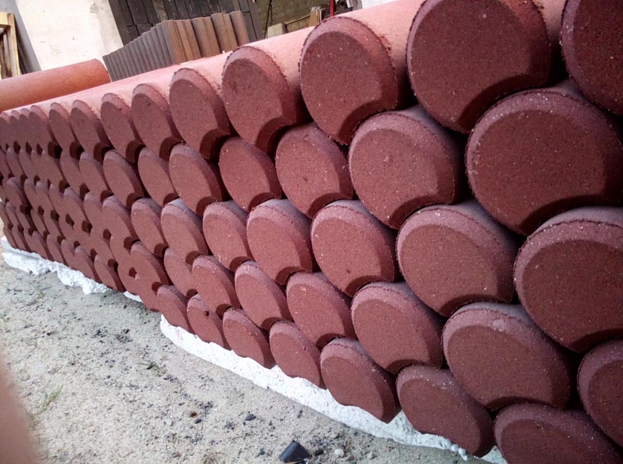 Czerwone, półokrągłe elementy betonowe ułożone warstwami, prawdopodobnie fragment ogrodzenia, widoczne ślady piasku.