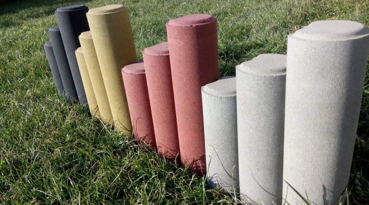 Prezentacja kolorystyki betonowych słupków ogrodzeniowych o cylindrycznym kształcie i zaokrąglonych wierzchołkach, ustawionych w rzędzie na trawie.