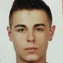 Portret młodego mężczyzny z kolczykiem w uchu, na jasnym tle. Widoczne bliskie ujęcie twarzy, z delikatnym oświetleniem.