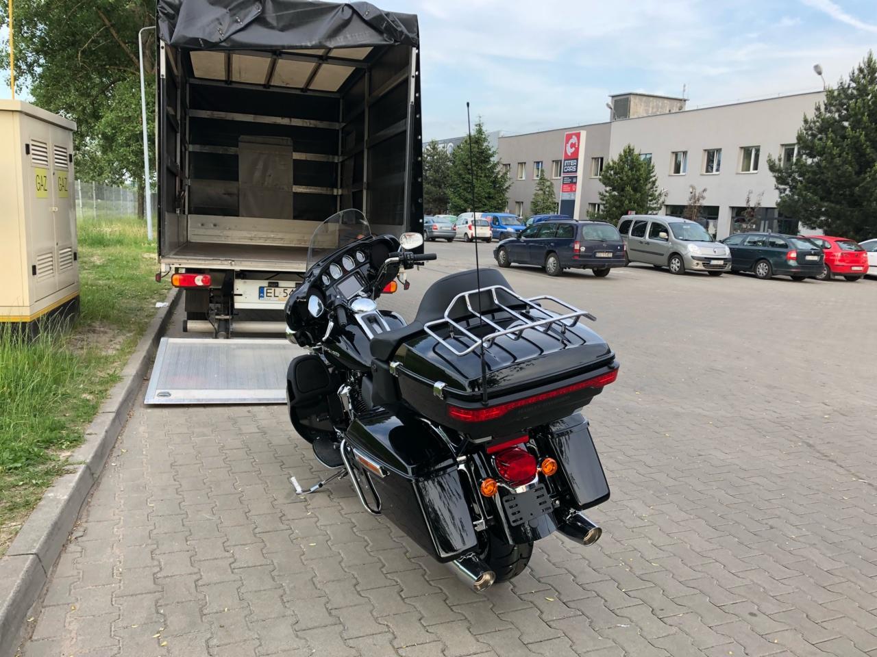 Czarny motocykl Harley Davidson na rampie ciężarówki transportowej z otwartą plandeką, gotowy do załadunku.
