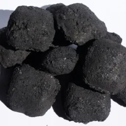 Kupa ekogroszku o nieregularnych kształtach, błyszcząca w świetle słonecznym, rzucająca cień na białe tło.