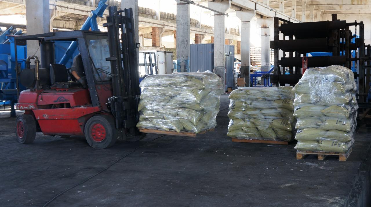 Czerwony wózek widłowy Linde transportuje paletę z workami zapakowanymi w folię stretch w hali magazynowej ze słupami i konstrukcją stalową