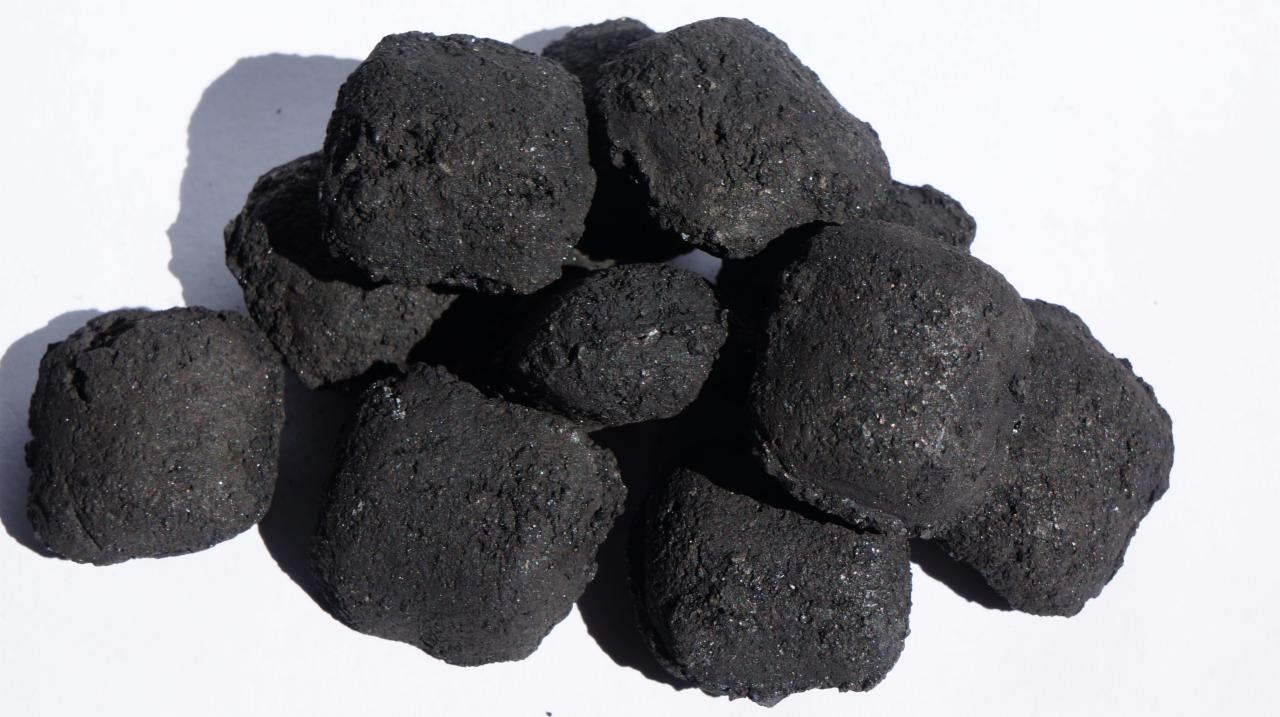 Kupa ekogroszku o nieregularnych kształtach, błyszcząca w świetle słonecznym, rzucająca cień na białe tło.