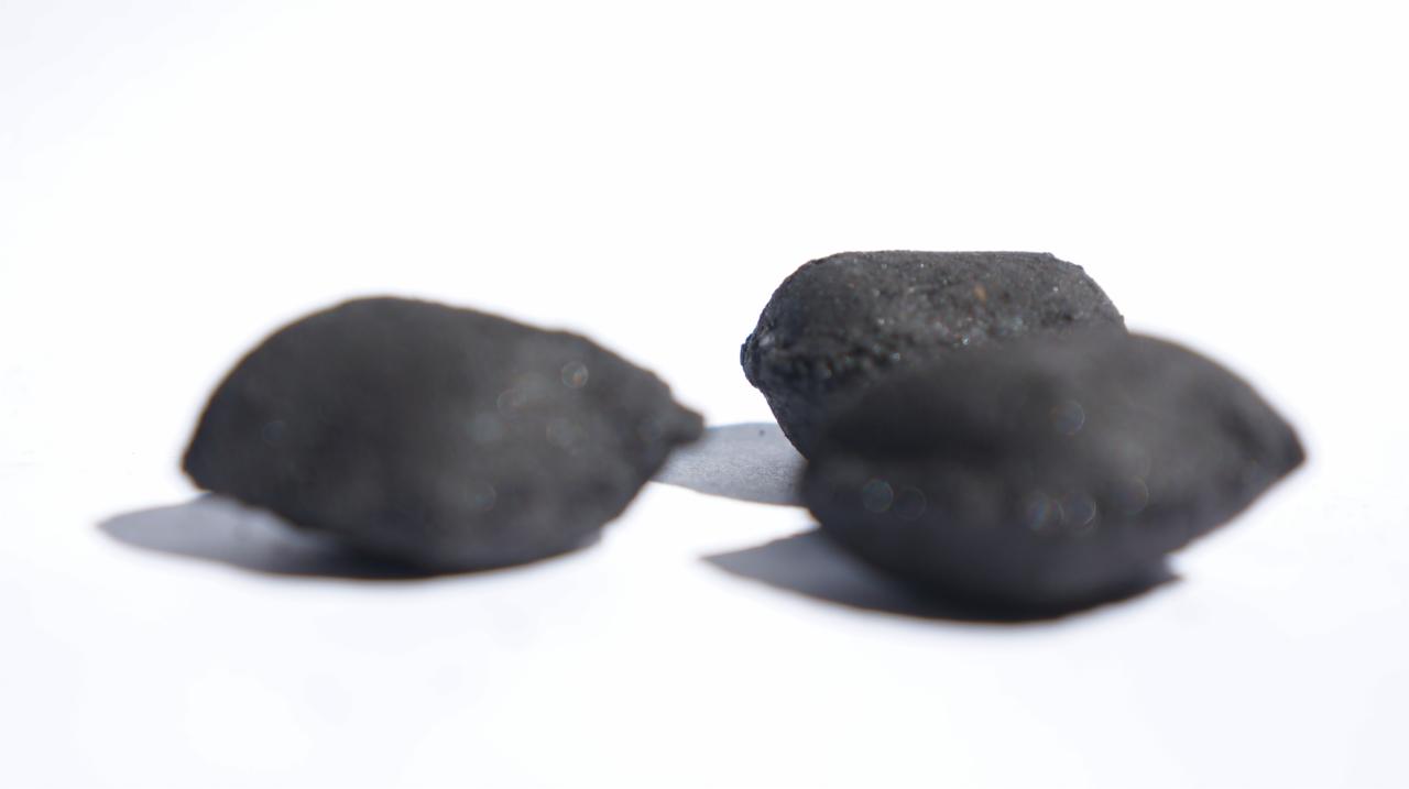 Trzy bryłki ciemnego paliwa stałego na białym tle, z widoczną fakturą i subtelnymi cieniami.