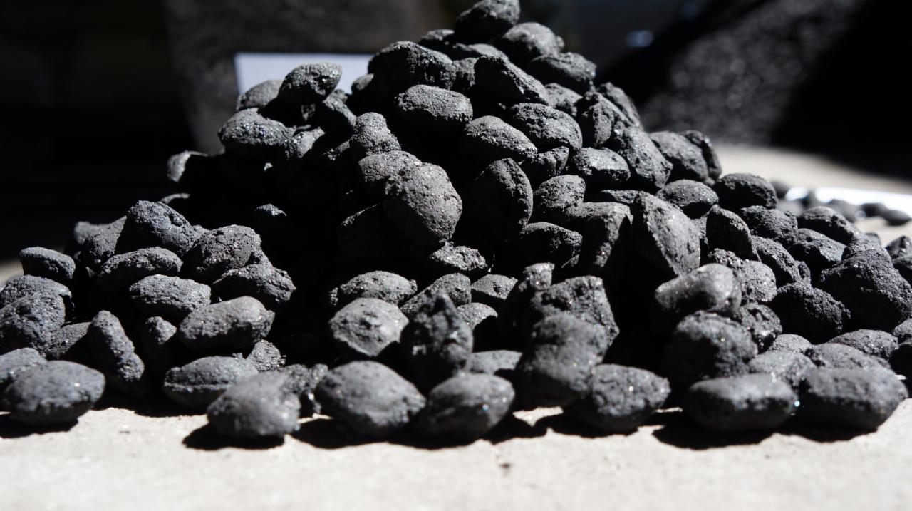 Kupa ciemnego, błyszczącego paliwa stałego na jasnej powierzchni w ostrym świetle, ukazująca nieregularne bryłki z widoczną strukturą.