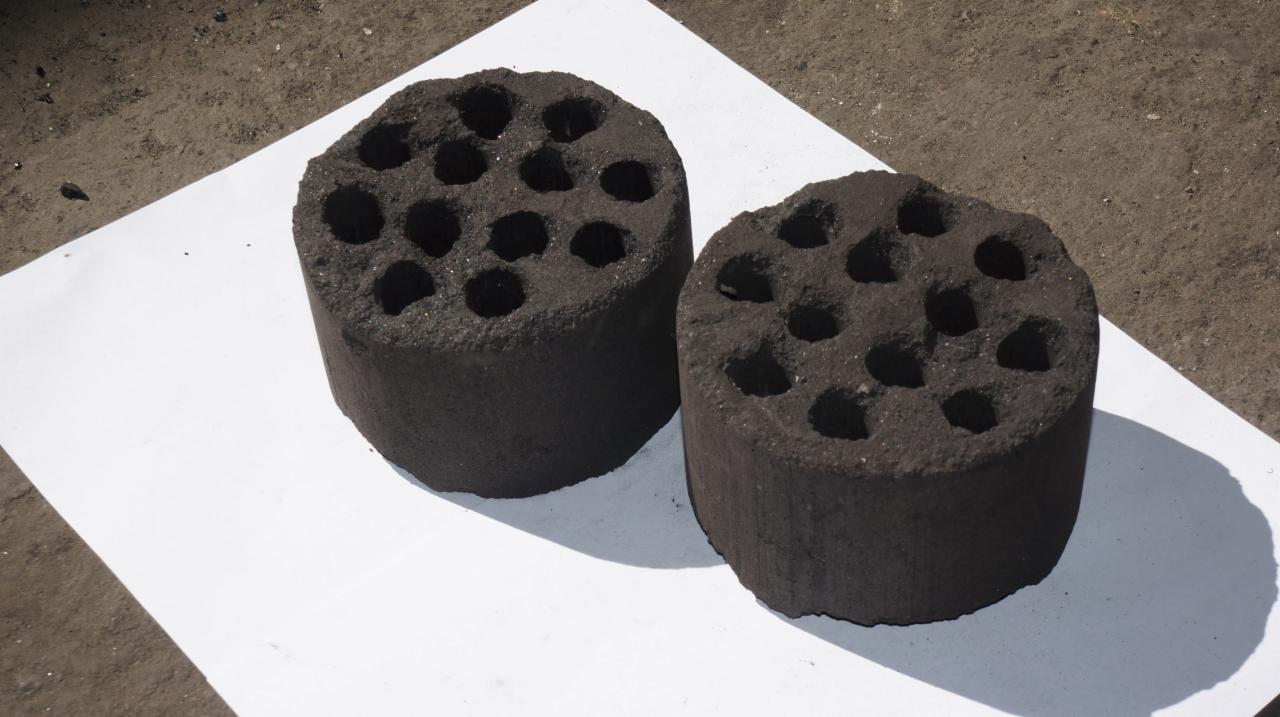 Dwa cylindryczne brykiety z otworami, ułożone na białym papierze na szarym, betonowym podłożu.