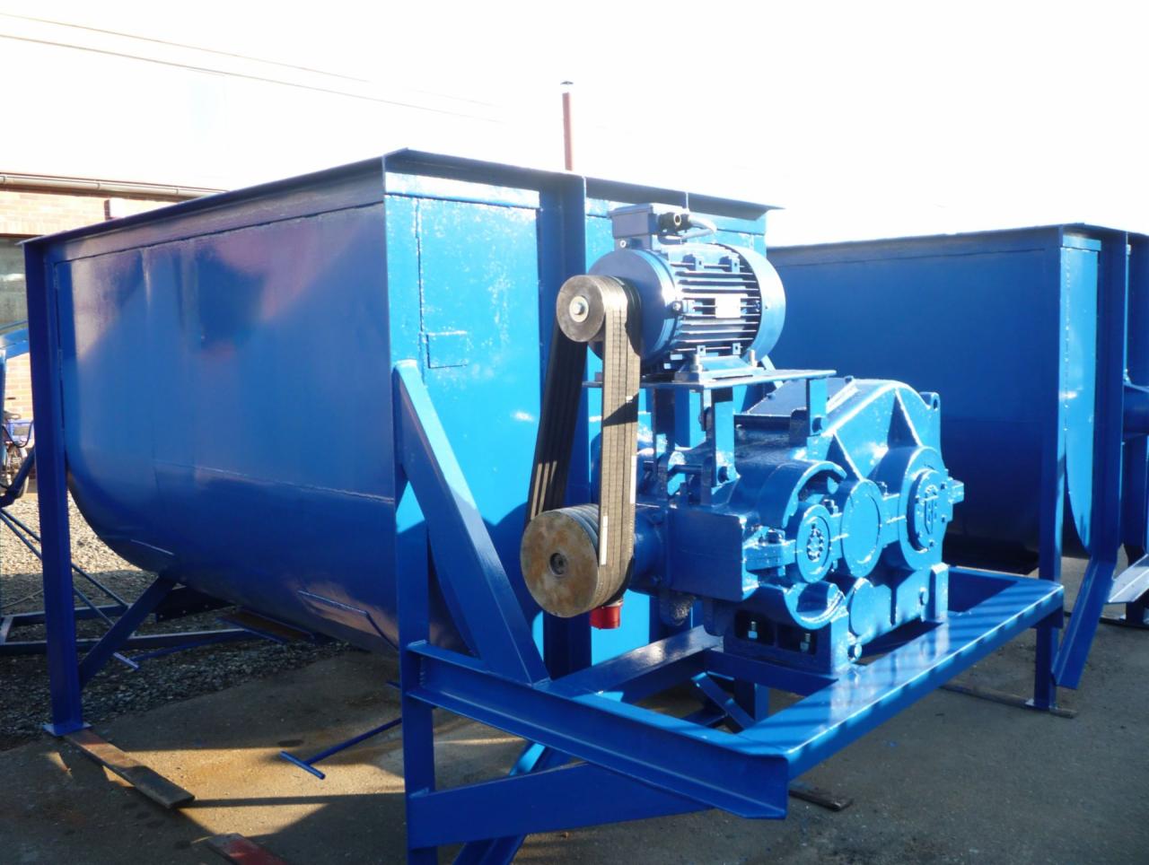 Niebieski mieszalnik przemysłowy z silnikiem i przekładnią pasową, ustawiony na betonowym placu, widoczne spawane konstrukcje nośne.