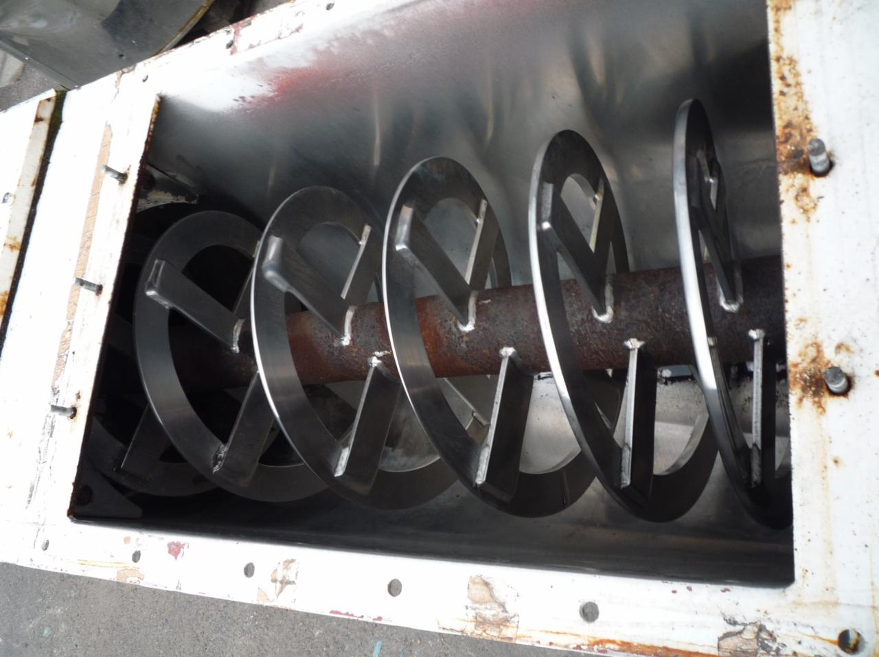 Wnętrze podajnika ślimakowego z metalowymi dyskami na rdzewiejącym wale, widoczne ślady użytkowania na obudowie.