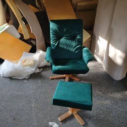 Zakład Tapicerski Feniks - Fotel obrotowy z podnóżkiem w odcieniach szmaragdowej zieleni, ustawiony w pomieszczeniu z widocznymi elementami pianki tapicerskiej w tle, sugerującym warsztat lub magazyn.