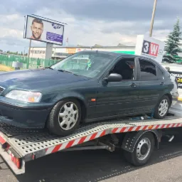 Zielony samochód Honda Civic transportowany na lawecie w Gdyni, widoczny billboard reklamowy i logo firmy holowniczej.