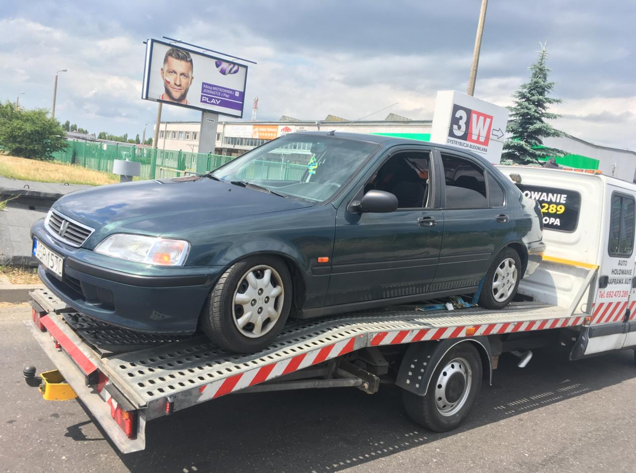 Zielony samochód Honda Civic transportowany na lawecie w Gdyni, widoczny billboard reklamowy i logo firmy holowniczej.