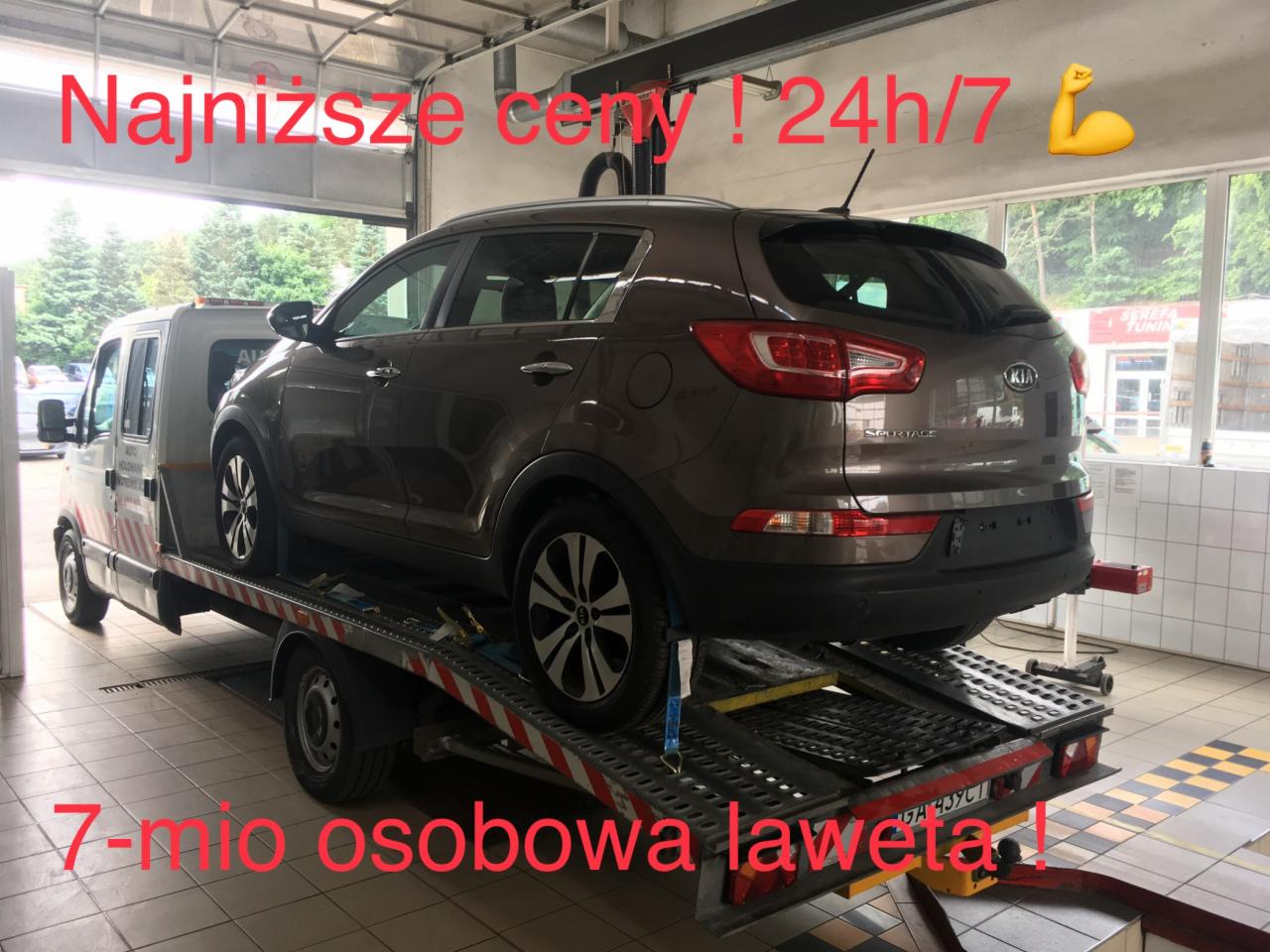 Brązowy samochód Kia Sportage załadowany na lawetę z napisem 'Najniższe ceny! 24h/7' i '7-mio osobowa laweta!' wykonana wewnątrz warsztatu.